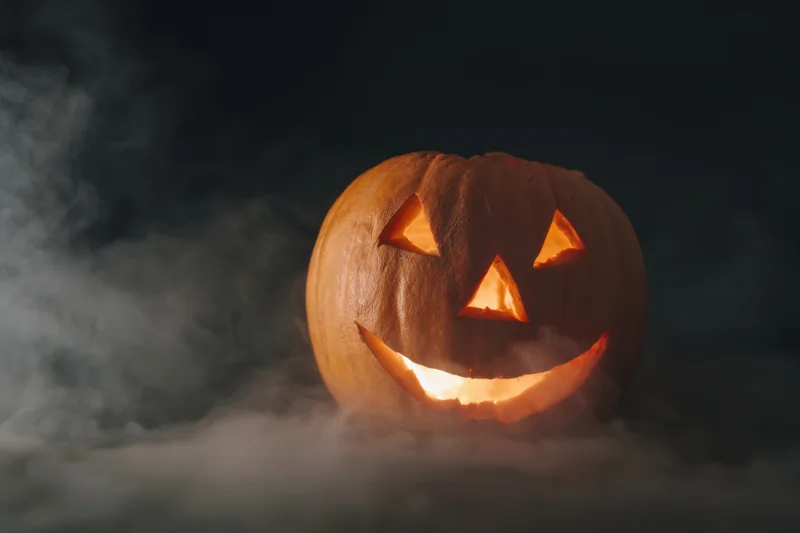 Glowing jack-o-lantern with carved face and eerie grin surrounded by smoke at night