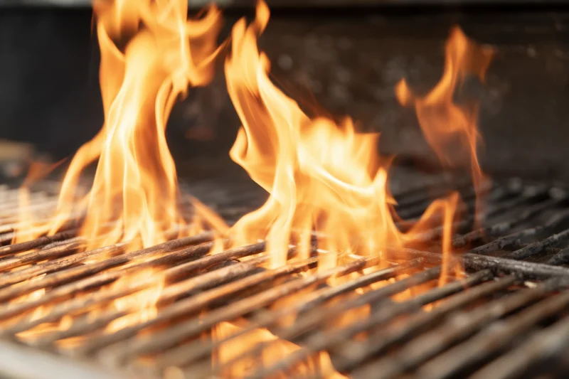 Bright flames rising between metal grill grates on an outdoor barbecue