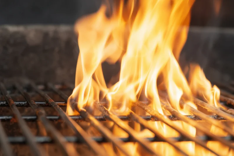 Bright flames rising between metal grill grates on an outdoor barbecue setup