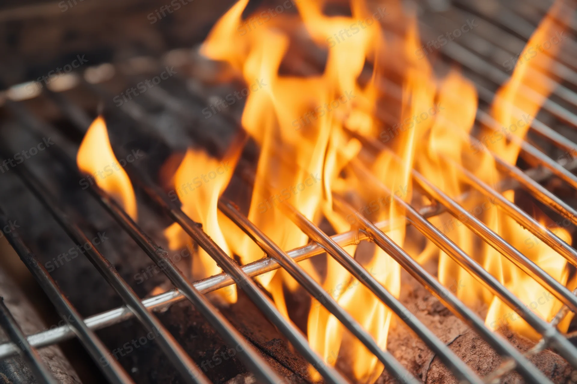 Bright flames rising between metal grates on a charcoal grill