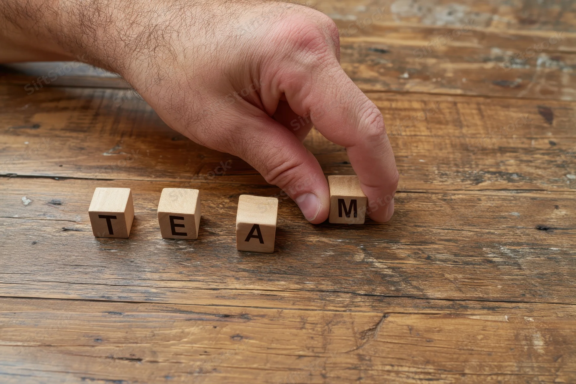 Hand placing wooden block with letter m to complete the word team on a rustic wooden table