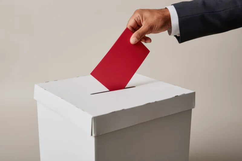Hand in suit casting red ballot into white ballot box