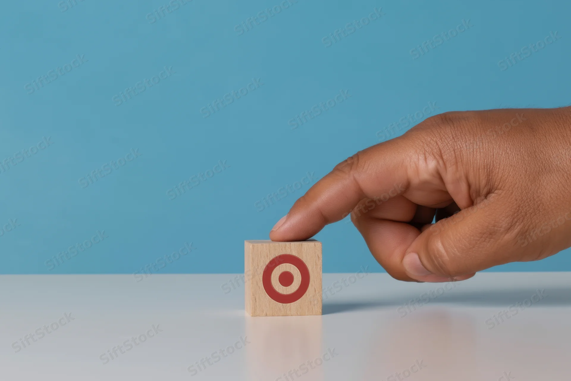 Hand placing wooden block with target symbol on white surface against blue background
