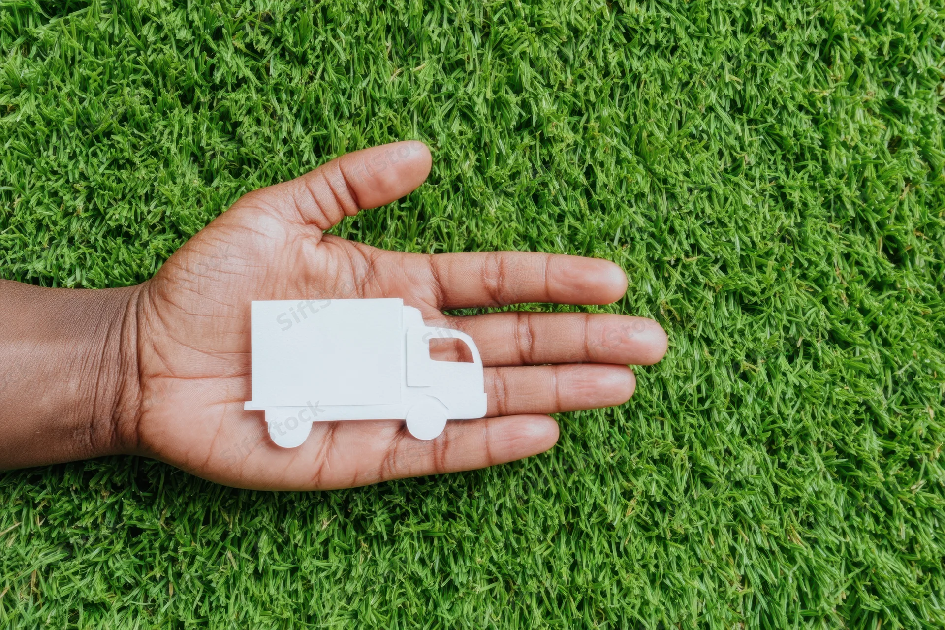 Hand holding a white paper cutout of a truck on a green grass background