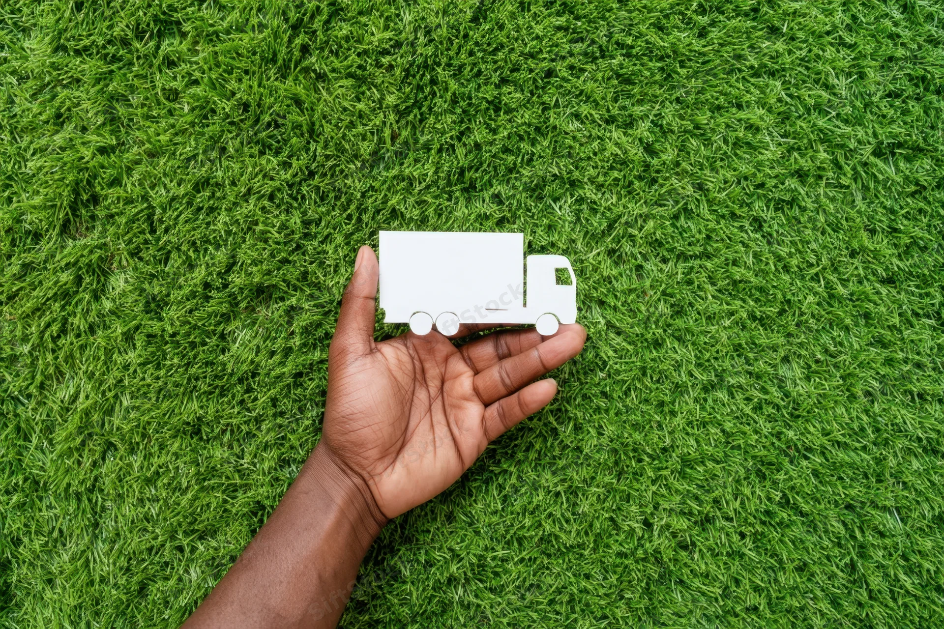 Hand holding a white paper cutout truck against a green grass background