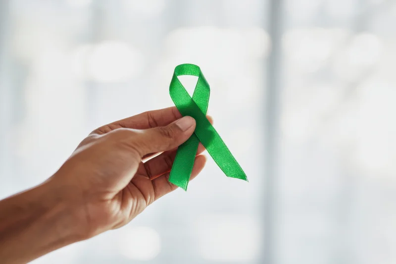 Hand holding green awareness ribbon against softly blurred background
