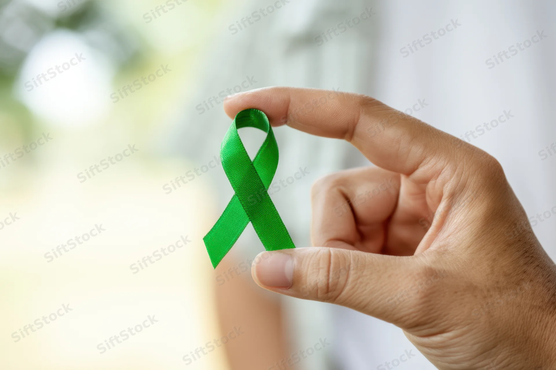 Hand holding green awareness ribbon against softly blurred background