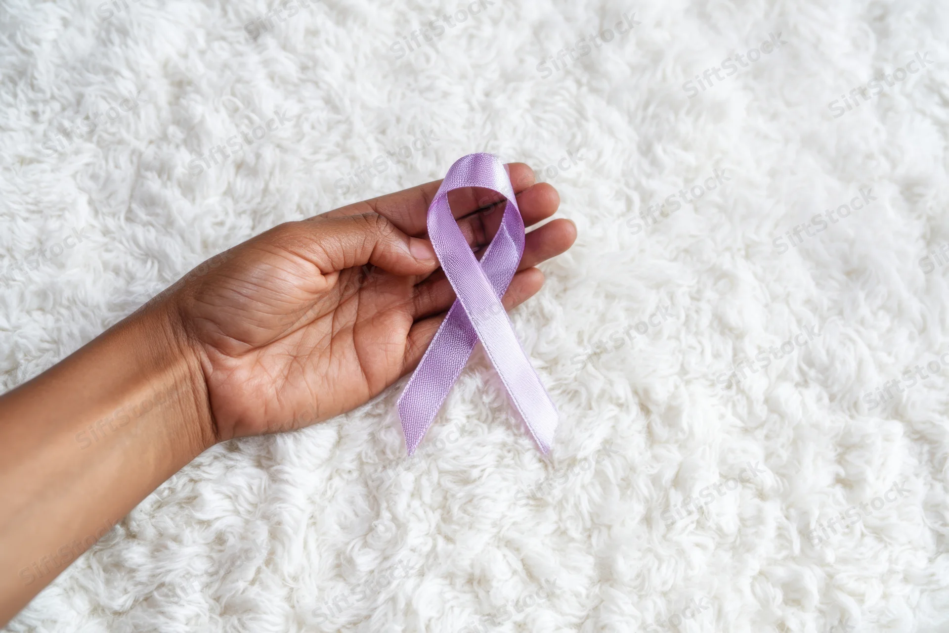 Hand holding lavender ribbon on white fluffy rug