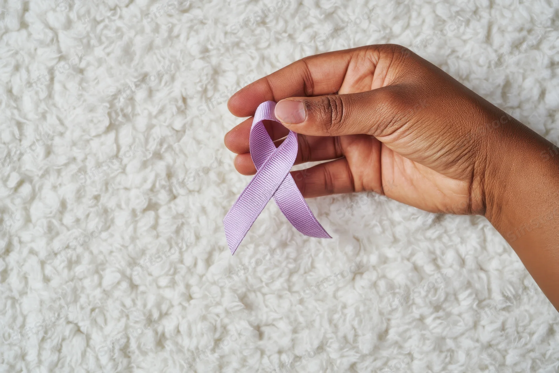 Hand holding a lavender ribbon against a soft fluffy white background