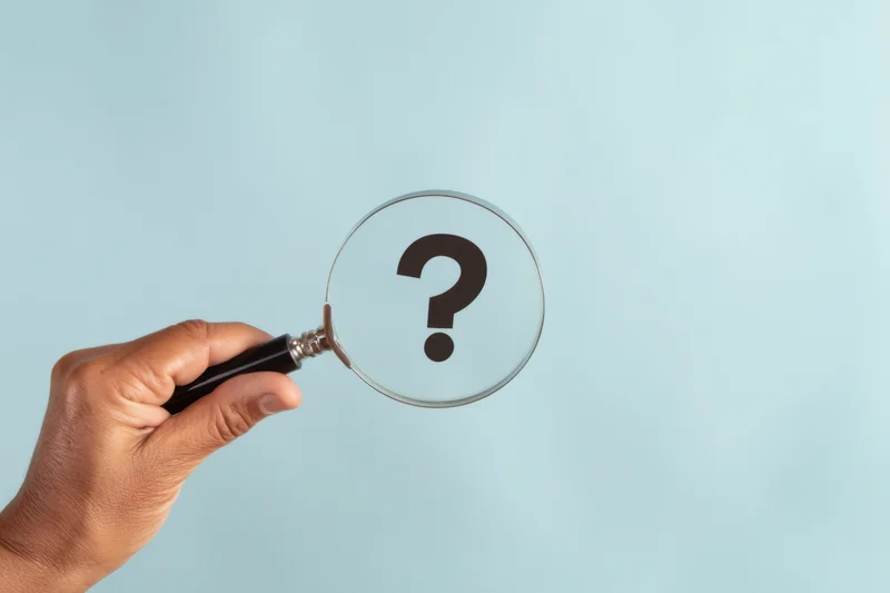 Hand holding magnifying glass over question mark against light blue background