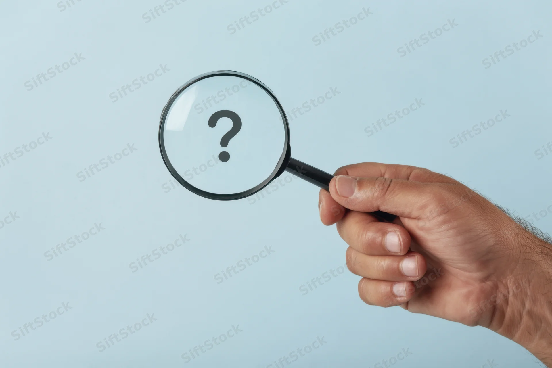 Hand holding magnifying glass with question mark against light blue background