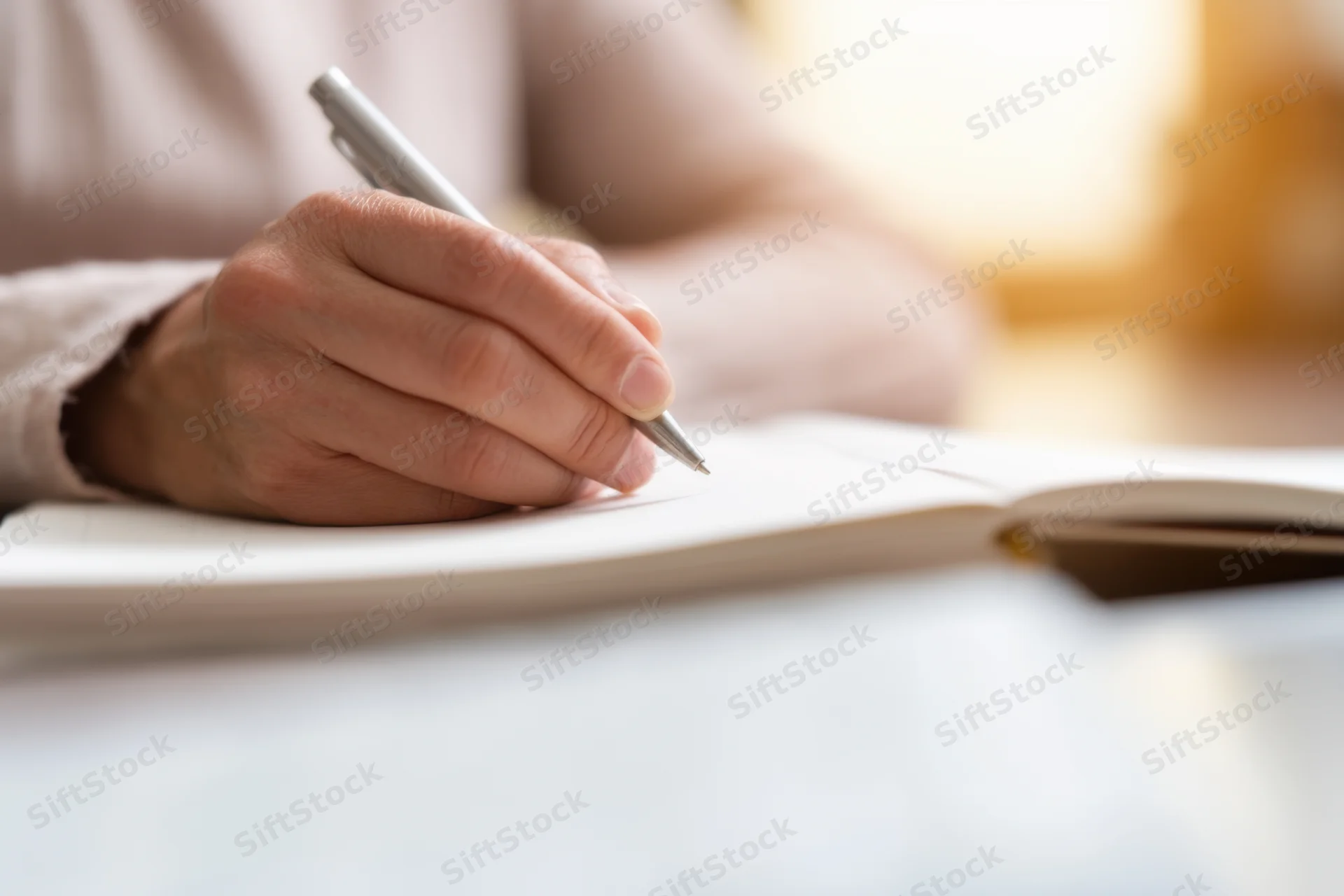 Hand holding pen writing in open notebook on desk