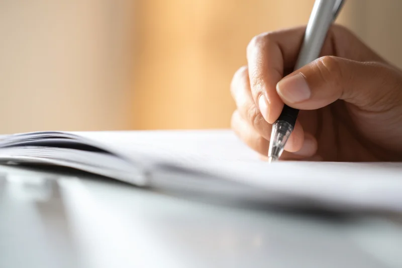 Hand holding pen poised over open notebook on desk