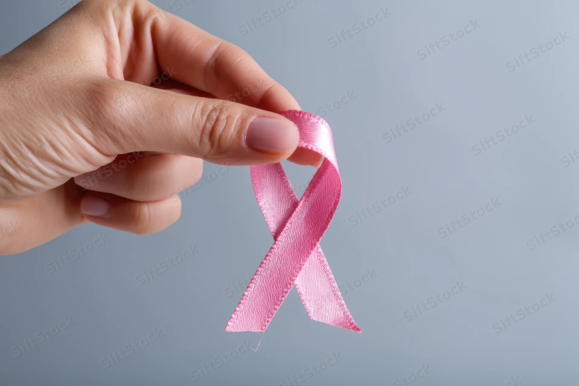 Hand holding pink ribbon against soft gray background