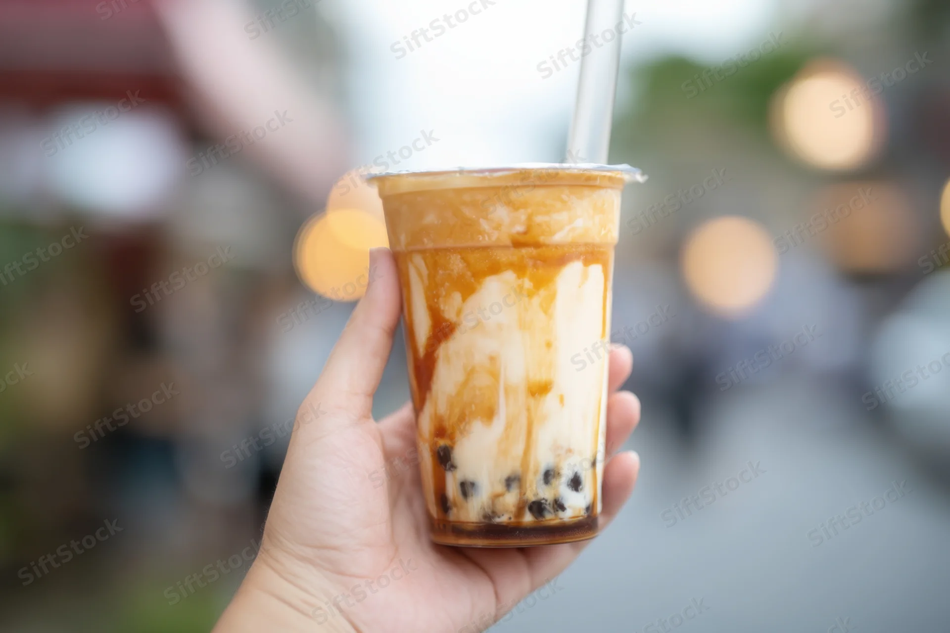Hand holding a layered bubble tea drink with tapioca pearls and caramel sauce outdoors