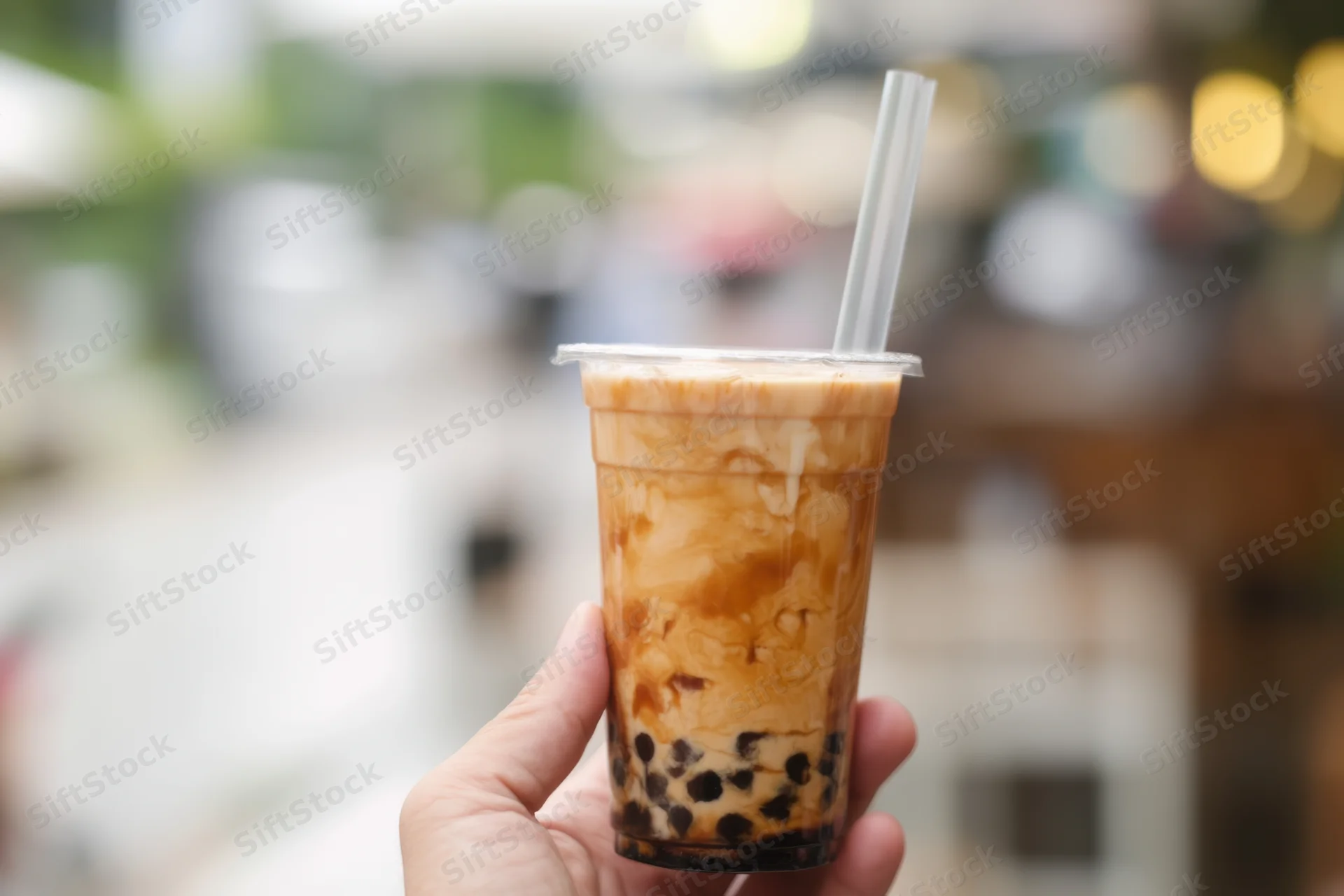 Hand holding a layered bubble tea drink with tapioca pearls and caramel swirl in a plastic cup outdoors