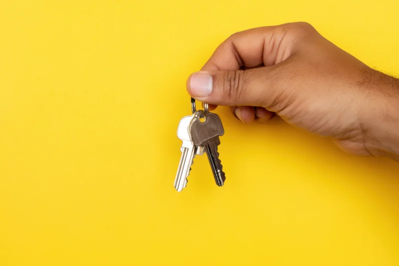 Hand holding keys against vibrant yellow background