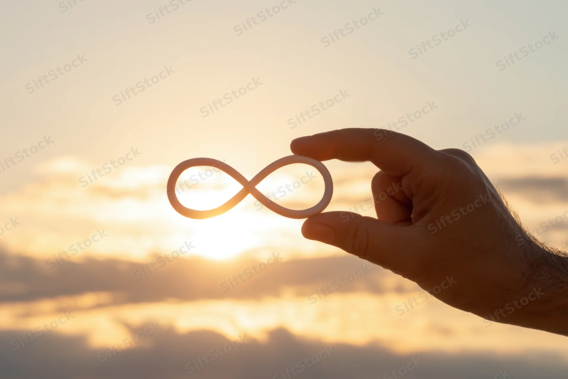 Hand holding infinity symbol against sunset sky