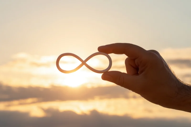 Hand holding infinity symbol against sunset sky