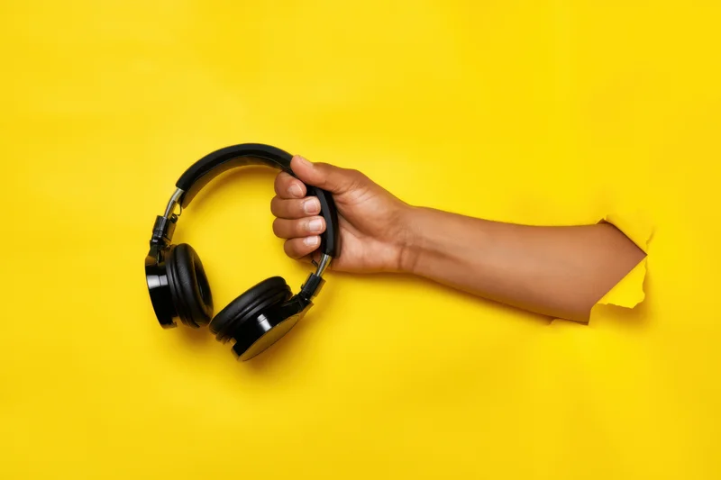 Hand reaching through torn yellow paper holding black headphones