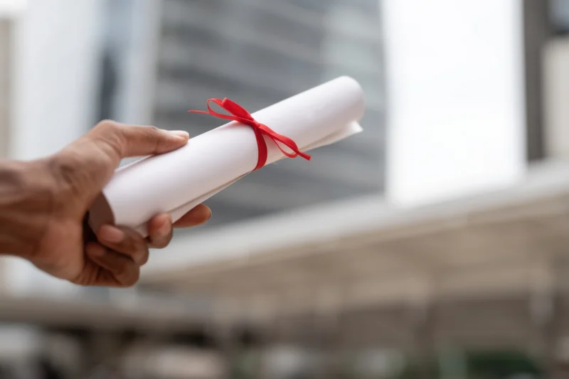 Hand holding rolled diploma tied with red ribbon outdoors