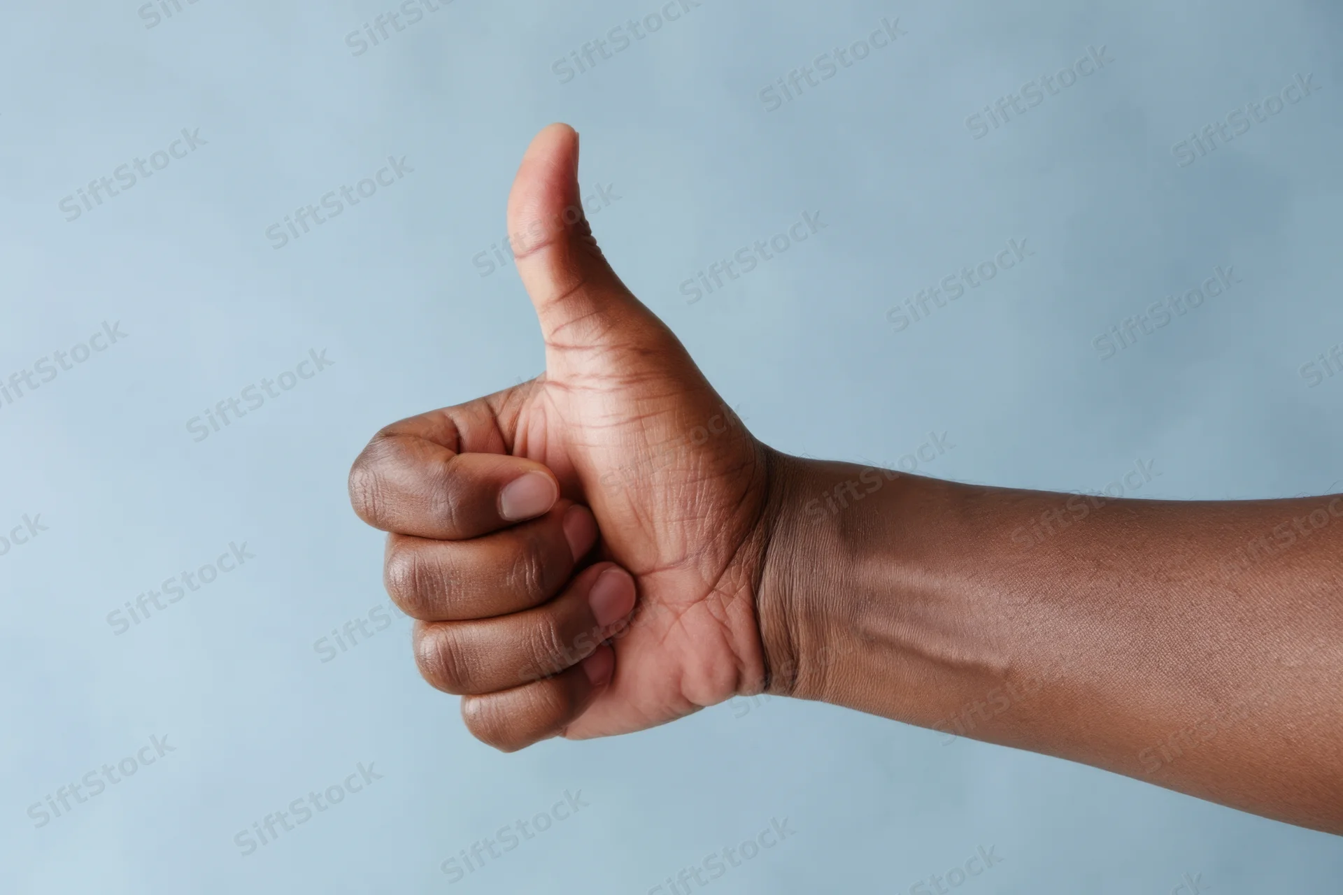 Hand making thumbs up gesture against soft blue background