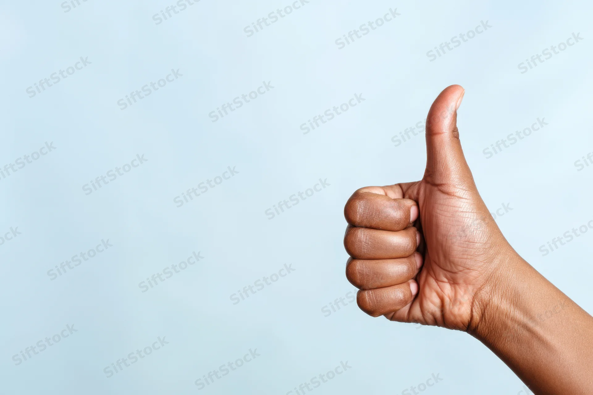 Hand making thumbs up gesture against soft blue background