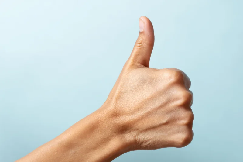 Hand making thumbs up gesture against soft blue background