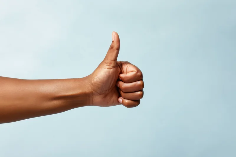 Hand making thumbs up gesture against soft blue background