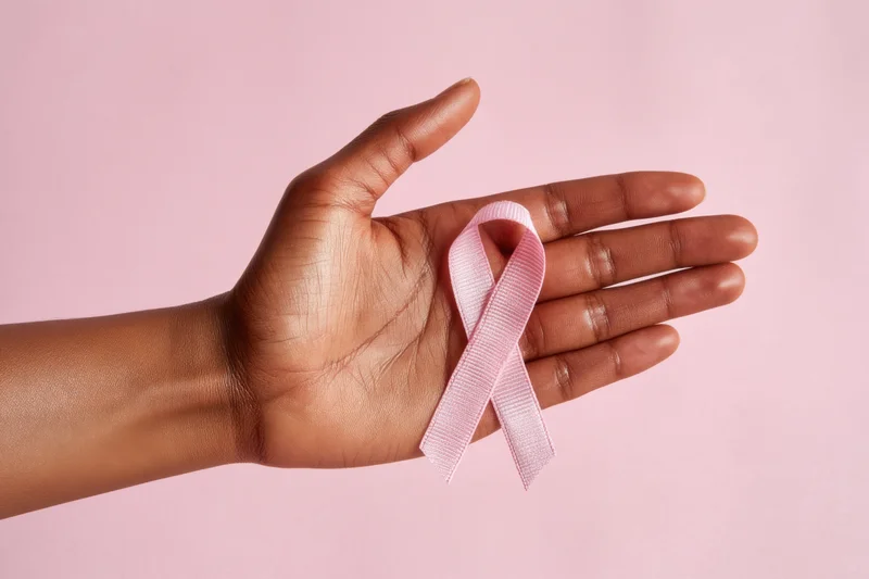 Hand holding pink ribbon against soft pink background