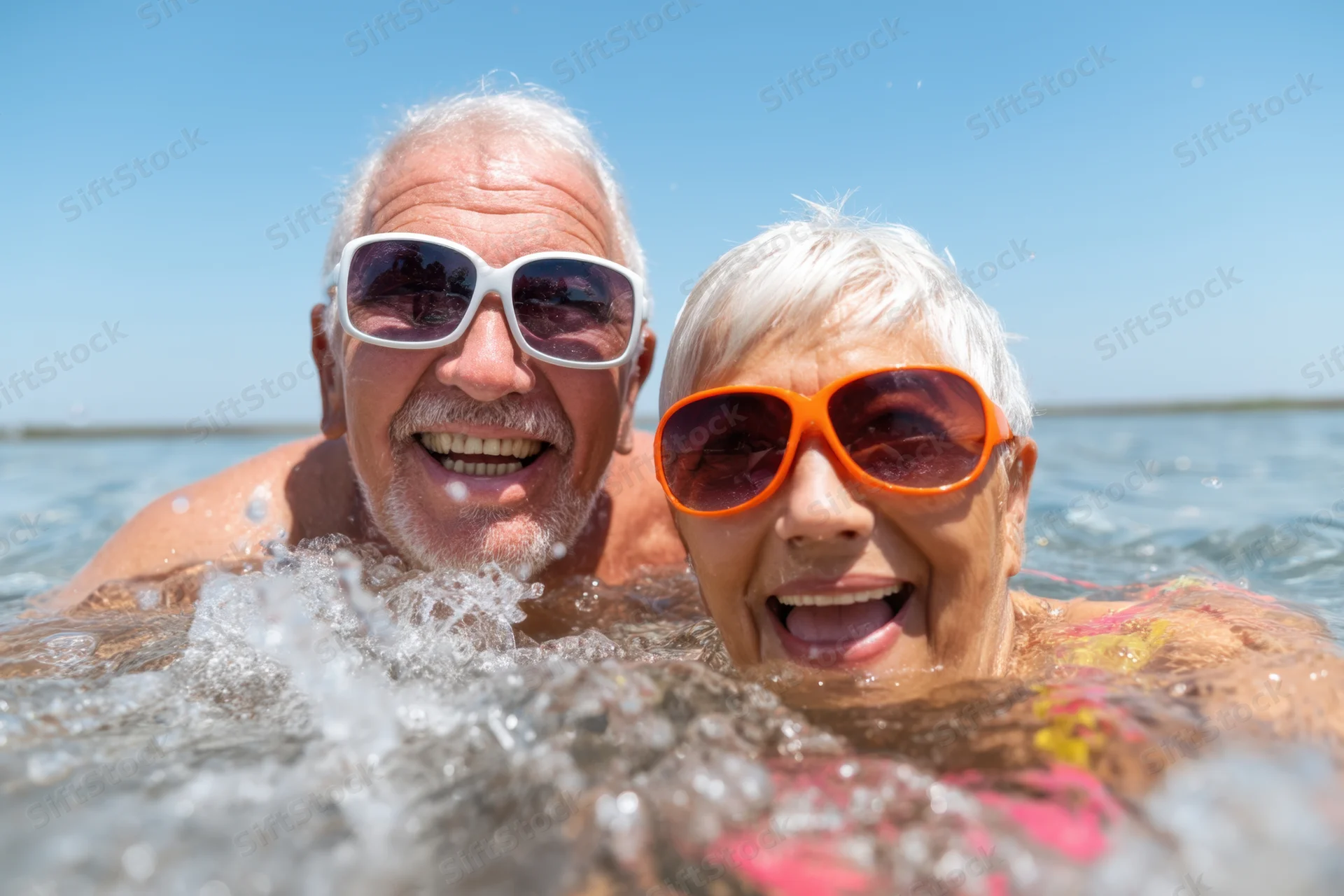 Elderly couple smiling in water at beach wearing sunglasses