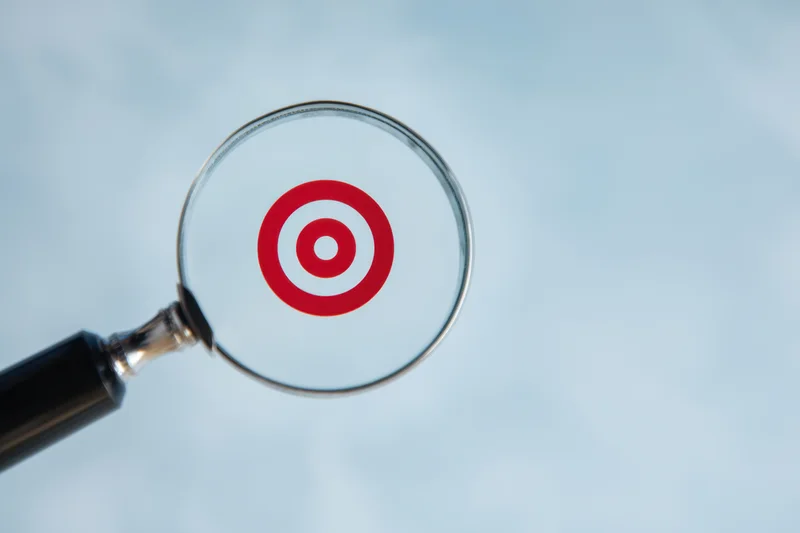 Magnifying glass focusing on a red target symbol against a light blue background
