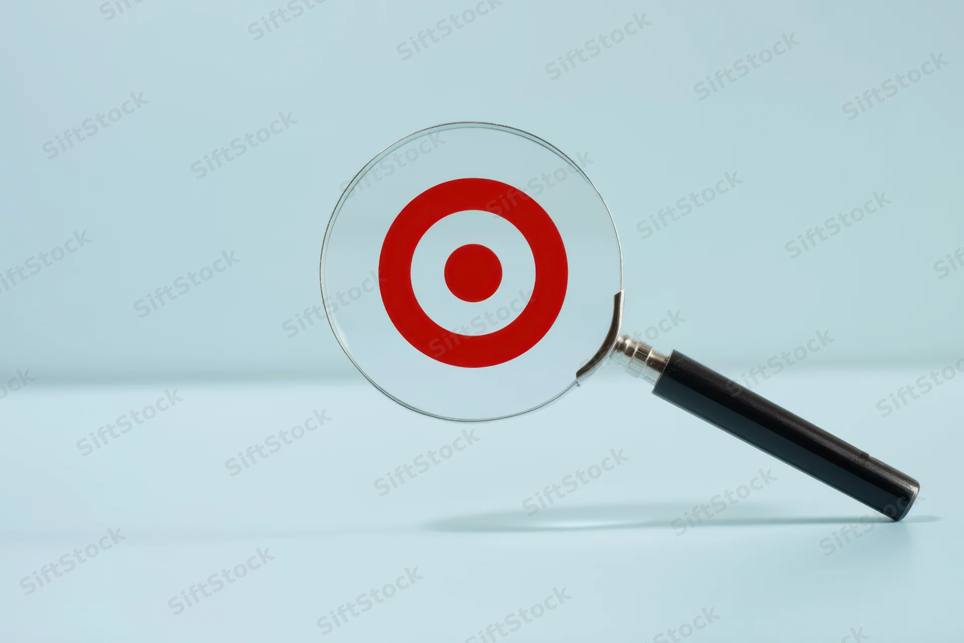Magnifying glass resting on a red target symbol on a light blue surface