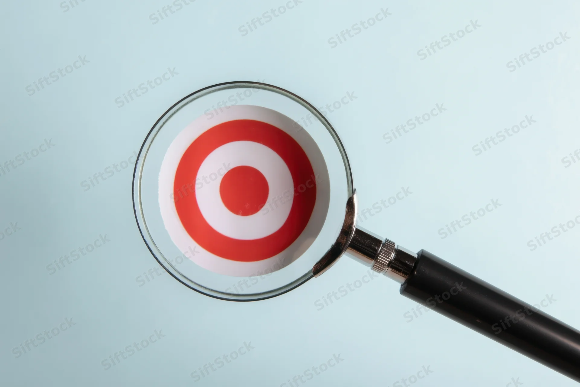 Magnifying glass focused on a red and white target symbol against a light blue background
