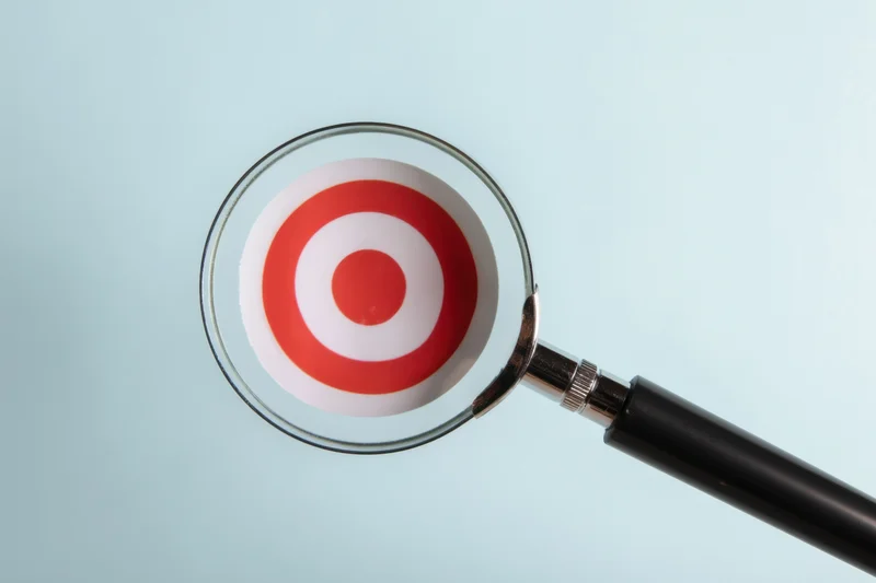 Magnifying glass focused on a red and white target symbol against a light blue background