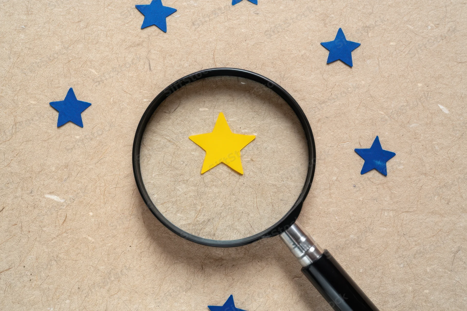 Magnifying glass focusing on a yellow star among blue stars on a textured beige surface