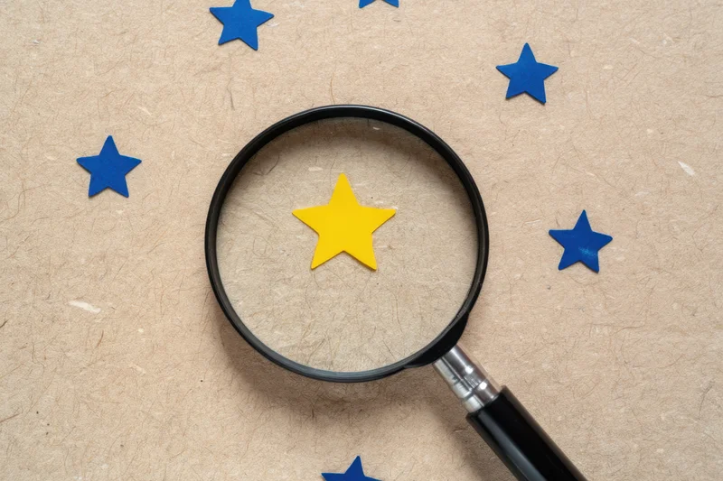 Magnifying glass focusing on a yellow star among blue stars on a textured beige surface