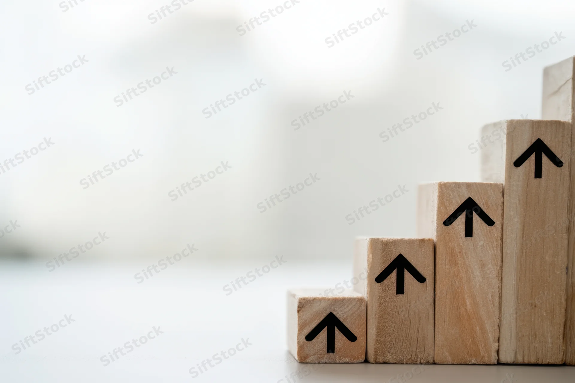 Wooden blocks with upward arrows arranged in ascending steps on a light surface