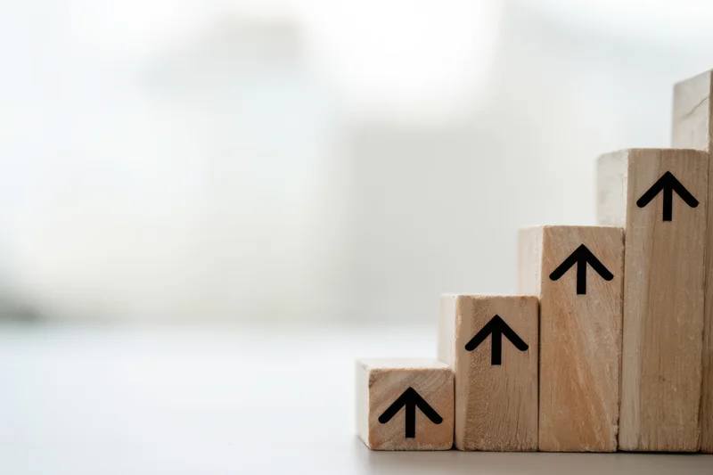 Wooden blocks with upward arrows arranged in ascending steps on a light surface