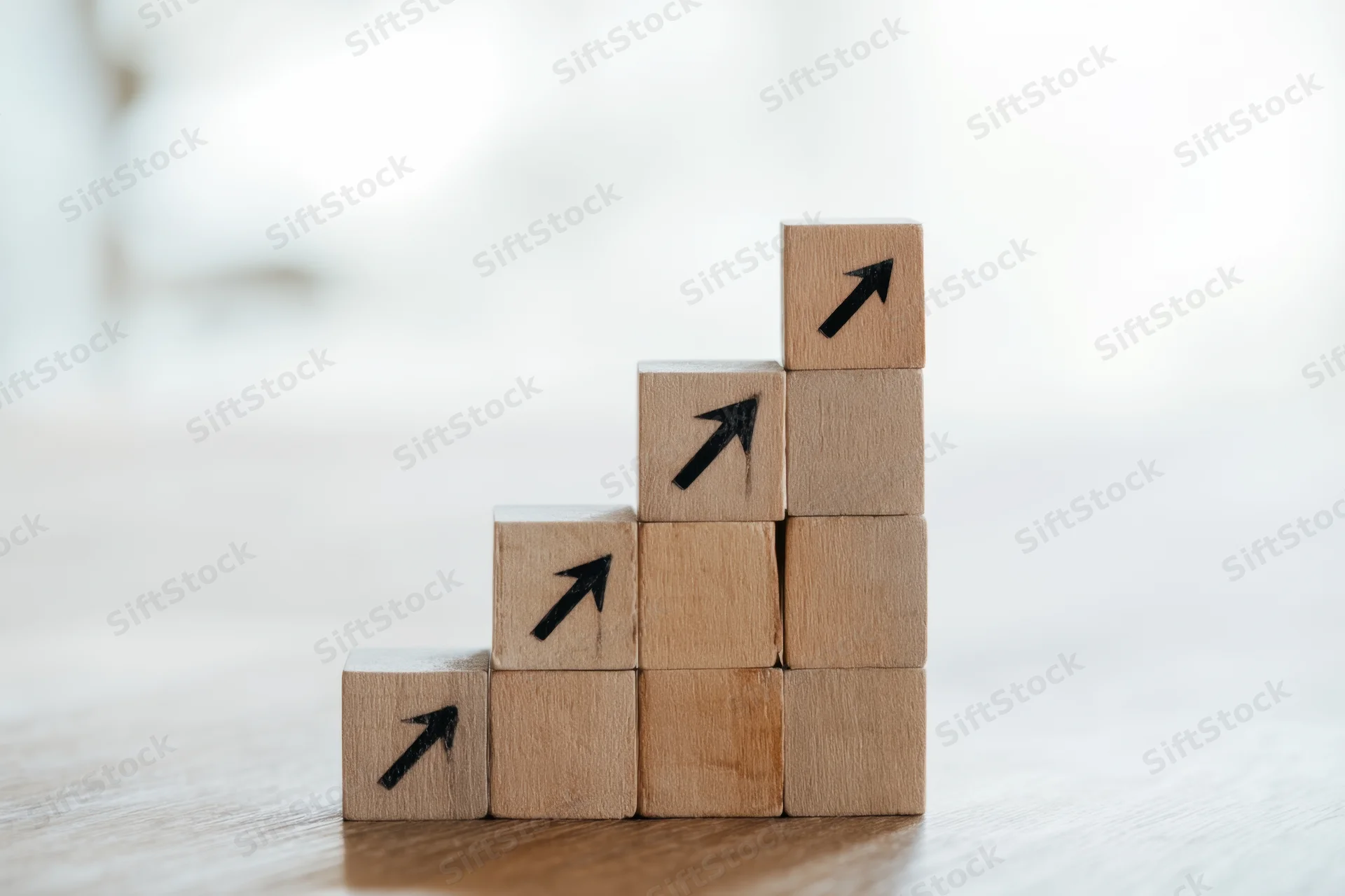 Wooden blocks arranged in a staircase with black arrows pointing upward on a wooden surface