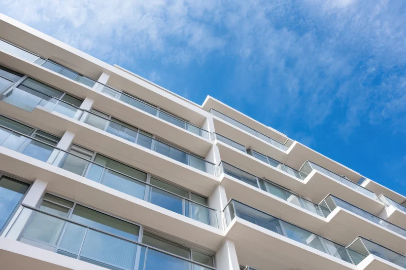 Modern apartment building exterior with white facade and glass balconies under blue sky
