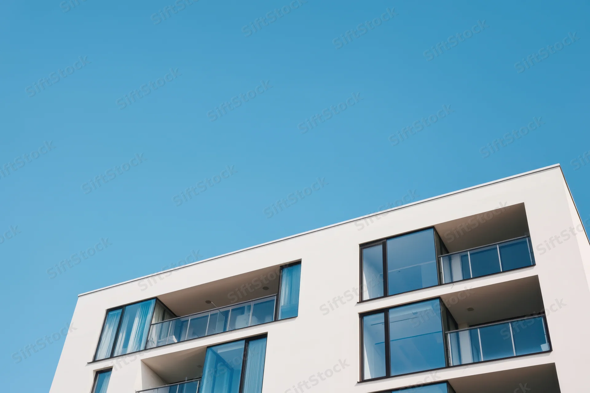 Modern apartment building with minimalist white facade and glass balconies under clear blue sky