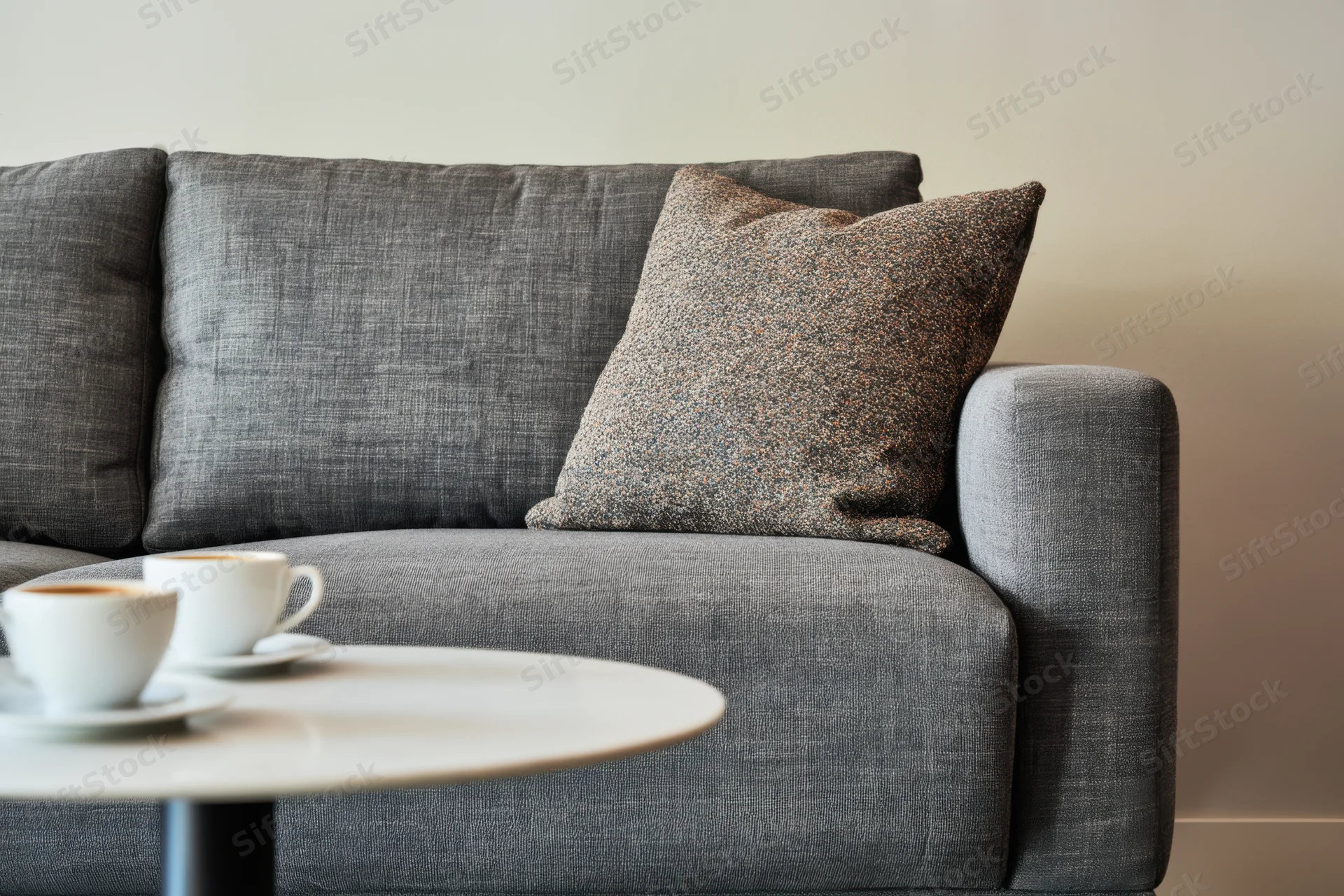 Gray modern sofa with speckled decorative pillow and coffee cups on a white table in a living room