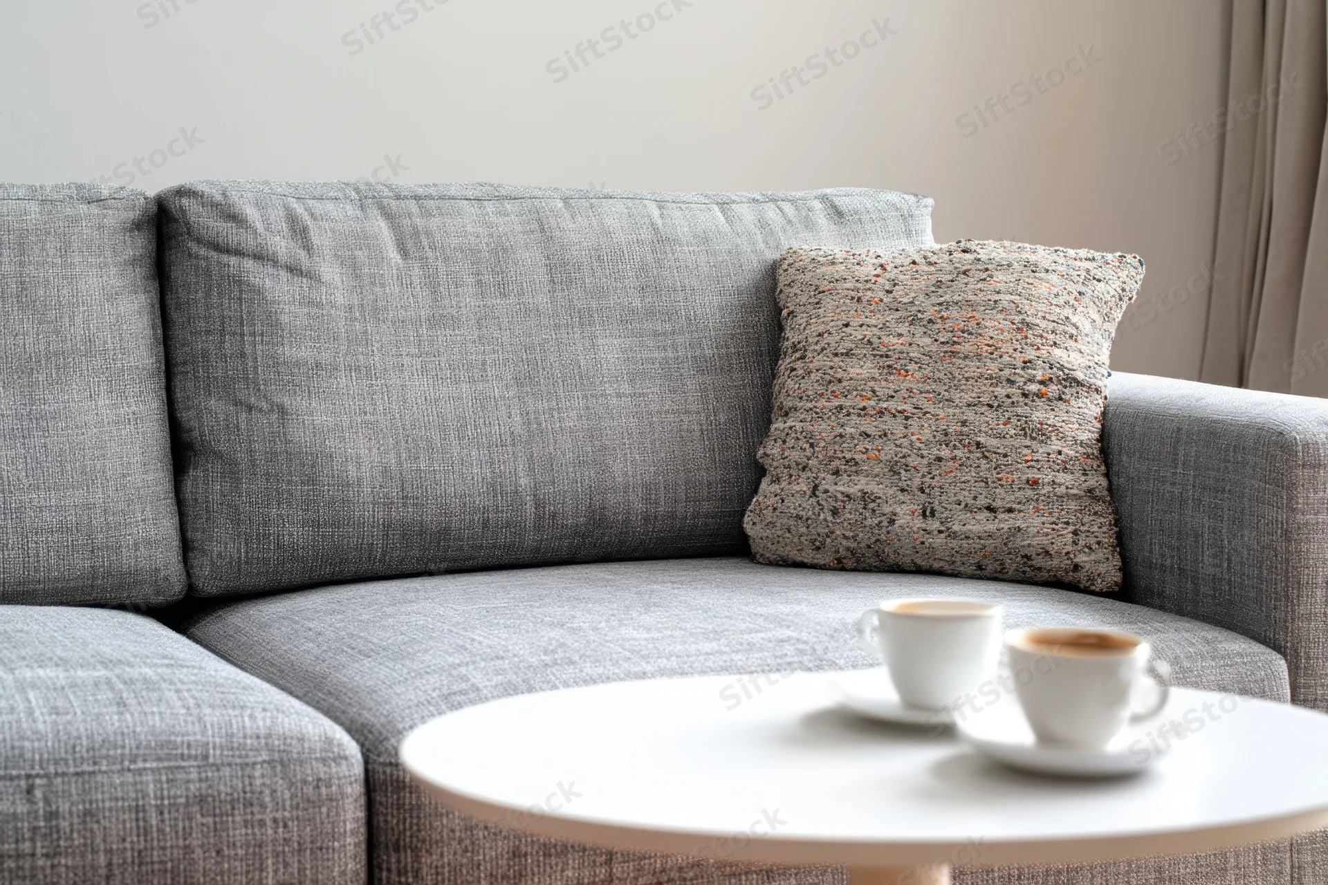 Gray modern sofa with decorative speckled pillow and coffee cups on round white table in living room