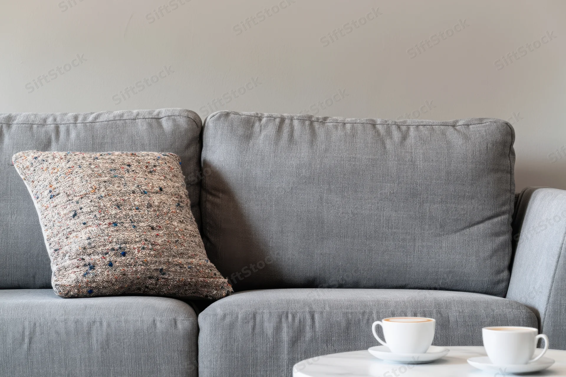 Gray sofa with speckled pillow and coffee cups on side table
