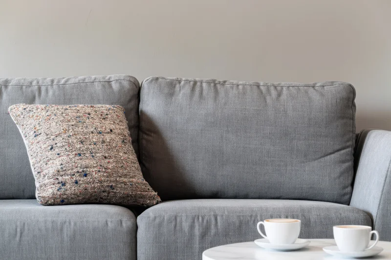 Gray sofa with speckled pillow and coffee cups on side table