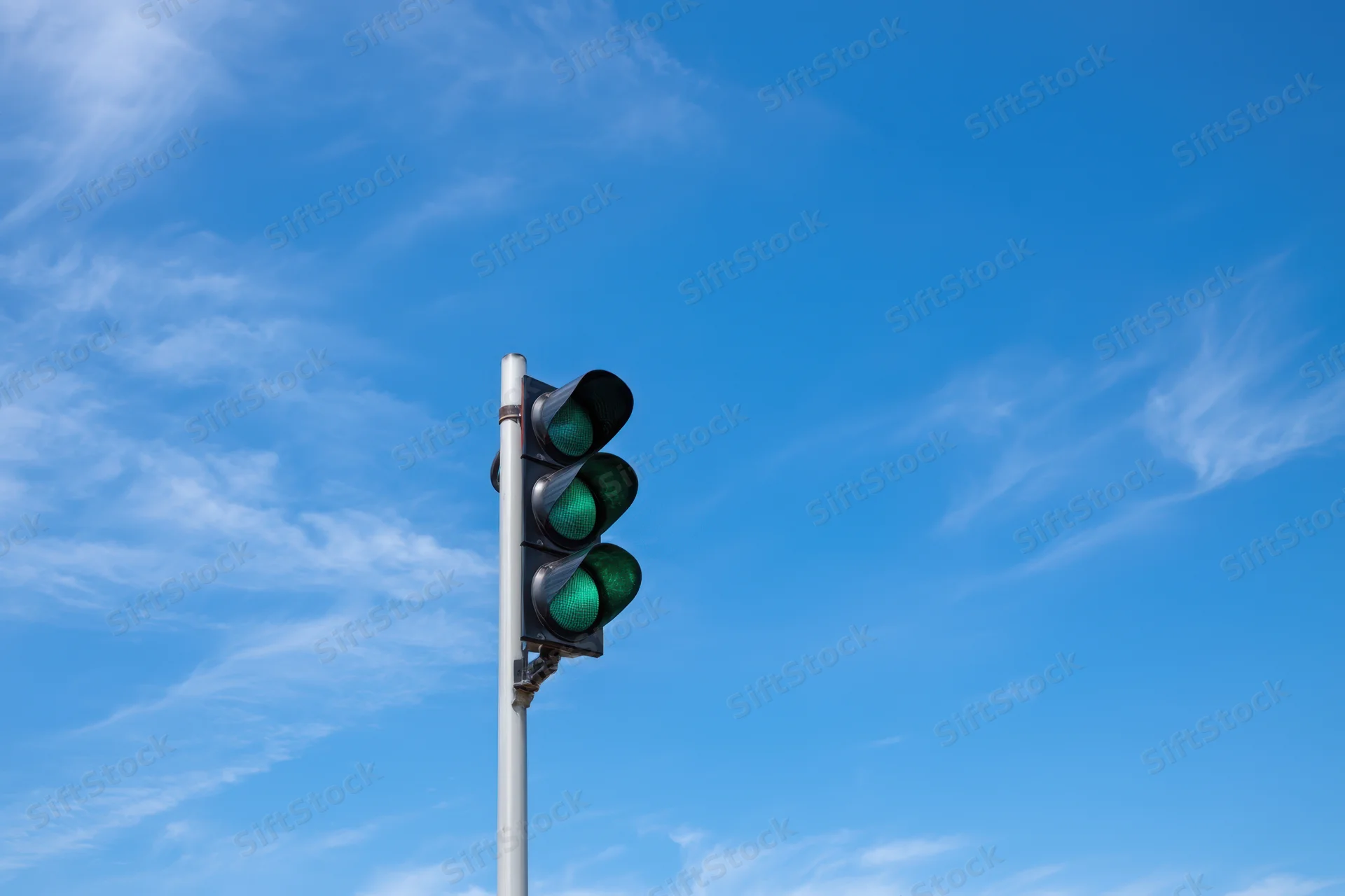 Modern traffic light with three green signals against a blue sky with wispy clouds