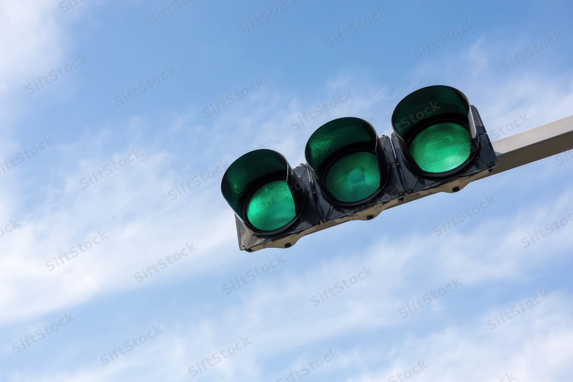 Three green lights on a modern traffic signal against a blue sky with scattered clouds
