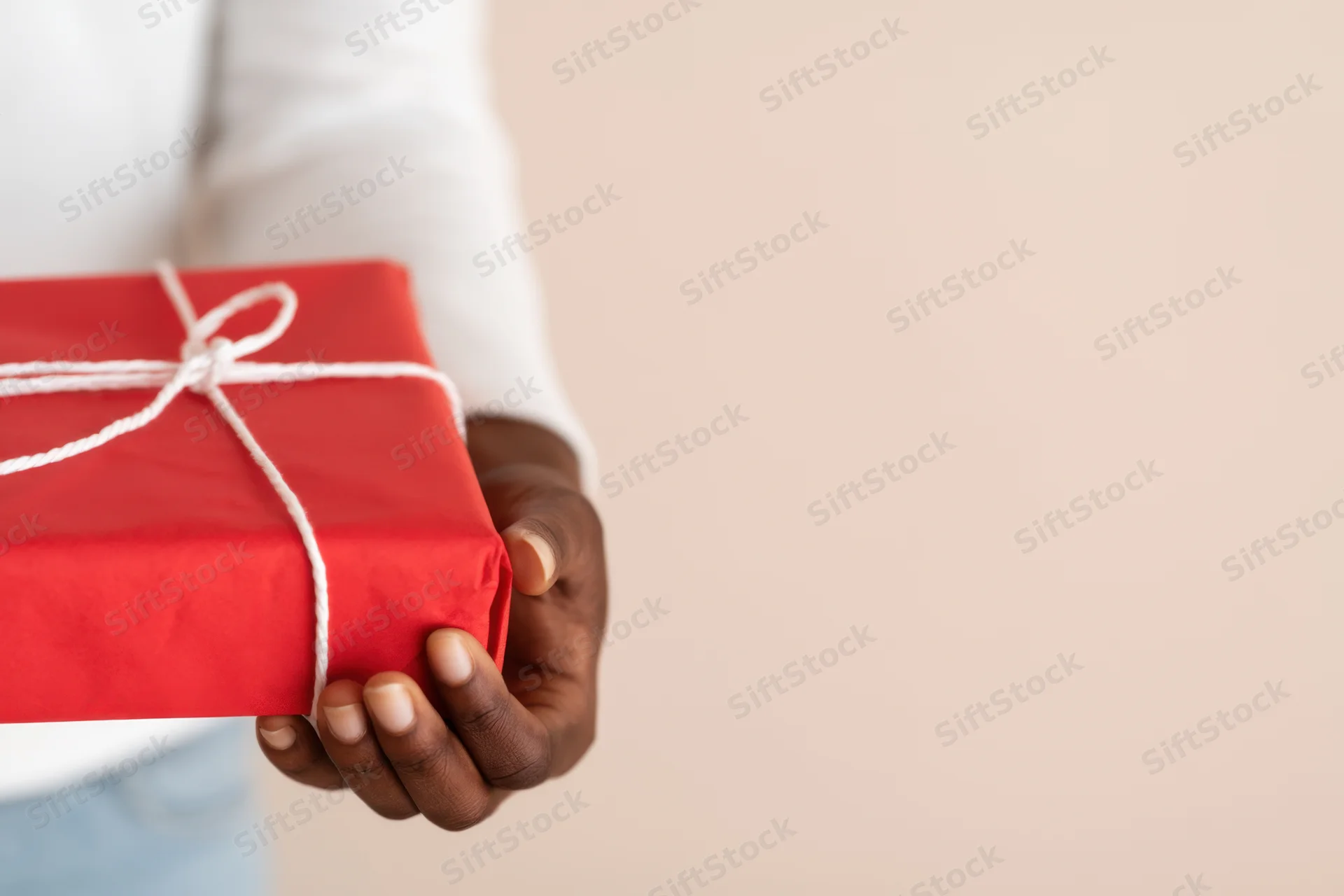 Hand holding a red gift box wrapped with white string against a plain background