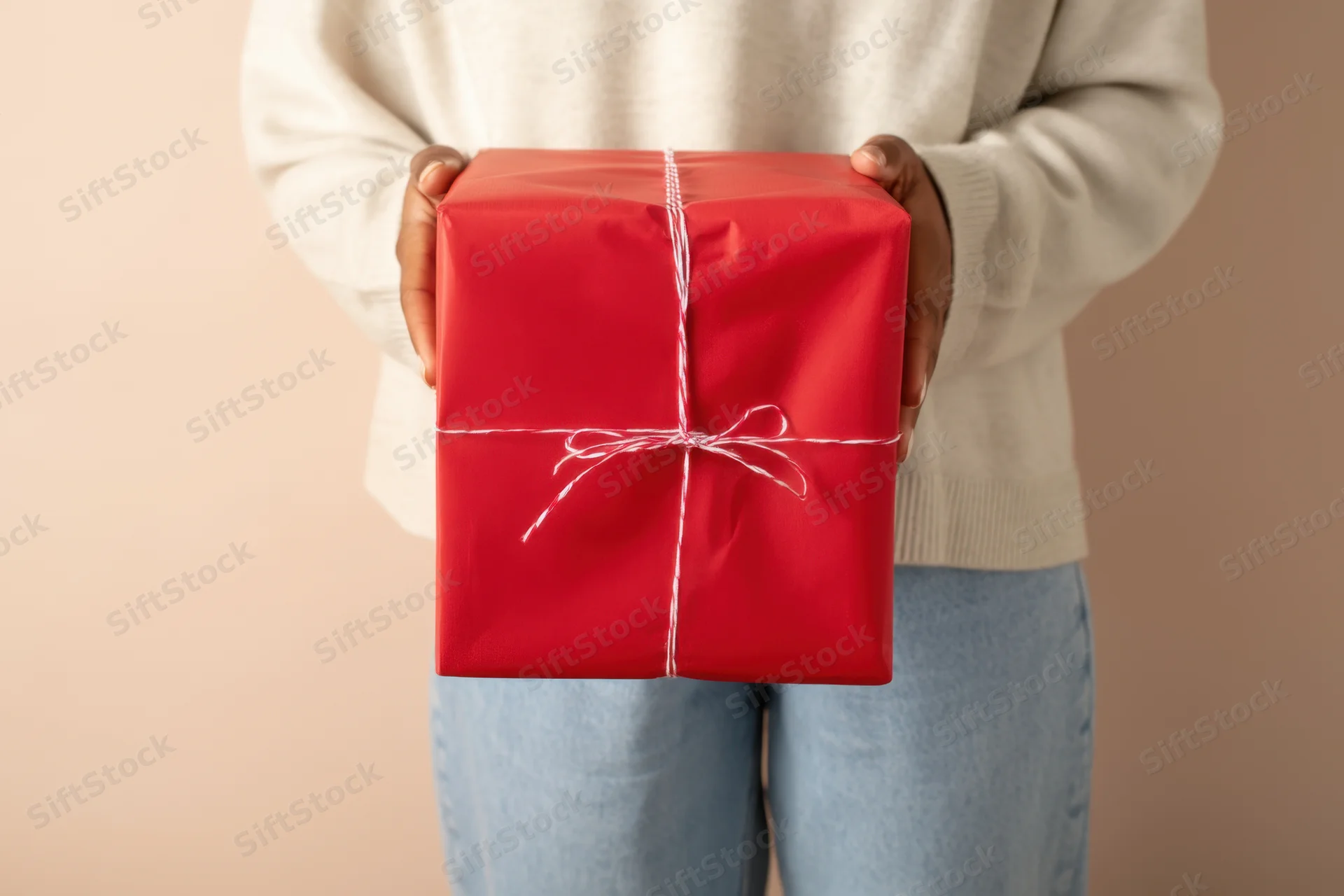 Woman holding a red wrapped gift box with white string bow in front of her body